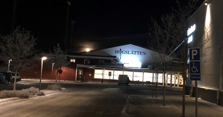 Exteriör bild på Högslättens ishalls entré kvällstid. Månen lyster över taket.