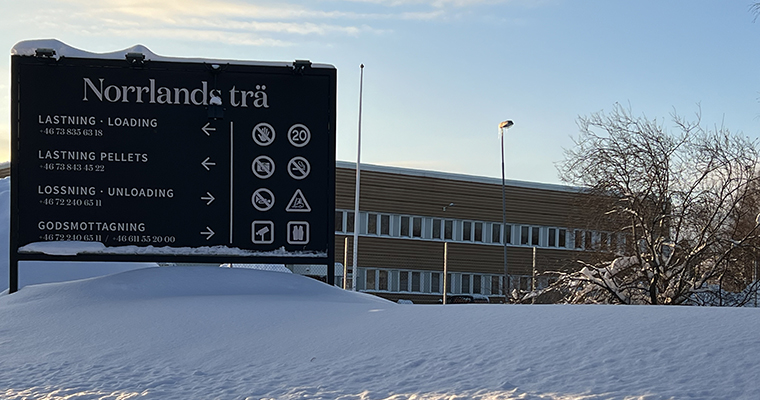 Stor skylt där det står Norrlands trä. I bakgrunden en stor byggnad i plåt.