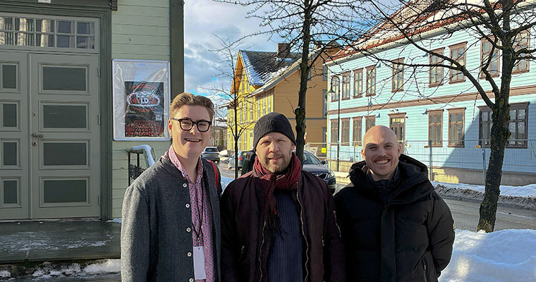tre personer står i en stadsmiljö med trähus