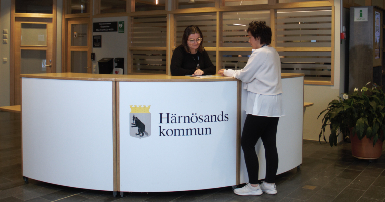 En kommunvägledare och en besökare vid en receptionsdisk, på disken finns Härnösands kommuns logga.