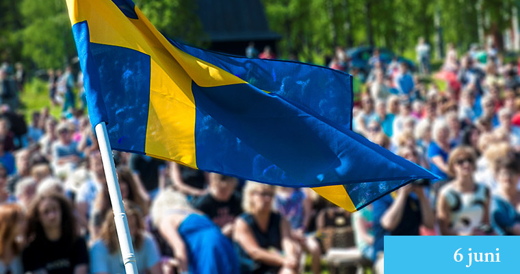 En svensk flagga med nationaldagsfirare i bakgrunden.