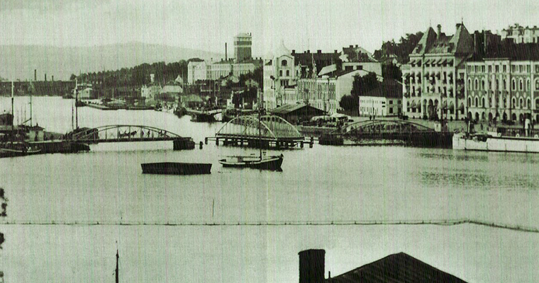 historisk bild i svartvitt på ett sund genom en stad. Över sundet leder en bågbro där mittendelen har vridits 90 grader och båtar passerar genom bron.