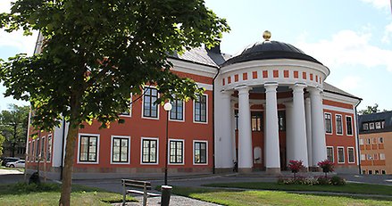 Exteriör bild på rådhuset i Härnösand. röd orange stenbyggnad med vita pelare.