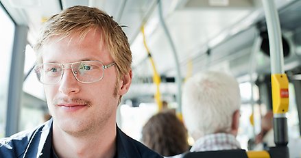 en medelålders man med glasögon och mustasch sitter på en buss